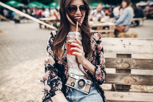 A woman holding a camera drinking lemonade.